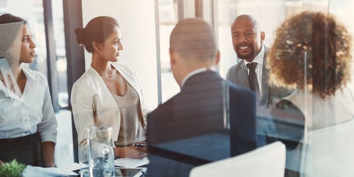 Three women and two men in business attire sitting at a boardroom table representing decision-making