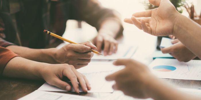Three sets of hands over a desk with paperwork representing assessing probability