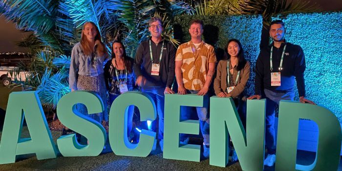 The resolver customer success team posing in front of the illuminated 'ascend' letters at ascend 2024, with a backdrop of palm trees and blue lighting.