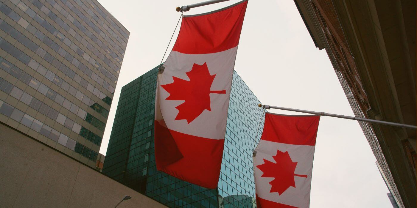 Two canadian flags are displayed in front of modern office buildings. The image relates to the osfi e-21 guideline on operational resilience and risk management.