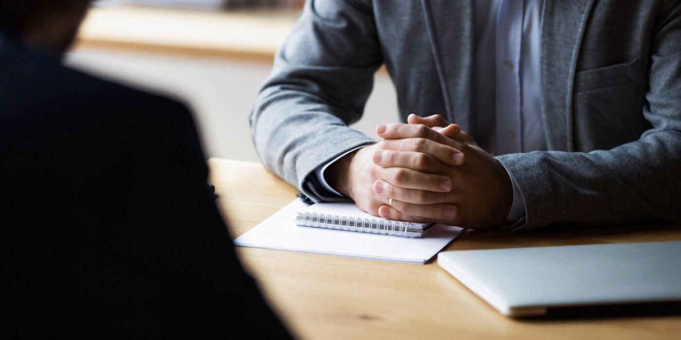 Close-up image of a professional sitting at a table with folded hands resting on a notebook, representing the concept of managing whistleblower cases.