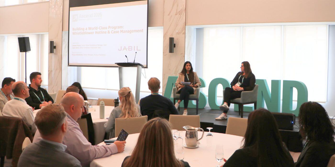 Speakers lead the jabil session at the ascend 2025 conference, titled "building a world-class program: whistleblower hotline & case management," as attendees listen around round tables with the word “ascend” displayed in large teal letters behind the stage.