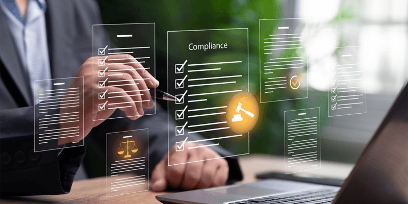 The image shows a professional seated at a desk working on compliance-related activities using a digital interface. Floating transparent panels display checklists, documents, and compliance records, with several items marked as completed. A central panel labeled “compliance” is prominently featured, surrounded by icons representing legal and regulatory functions, including a gavel and scales of justice. A laptop is visible on the desk, and the blurred office background suggests a modern workplace. The visual emphasizes digital compliance management, regulatory tracking, internal controls, governance processes, audits, and risk management in a business setting.